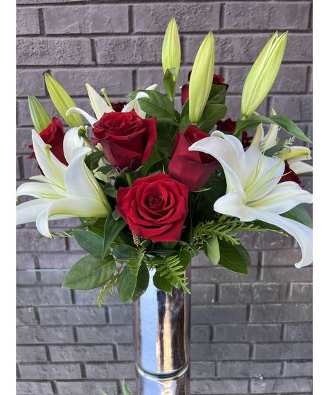 White lilies and pink roses wrapped with pink wire in a clear glass vase with pink gems.