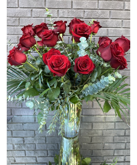 One dozen long stem red roses and greenery in a tall clear glass vase.