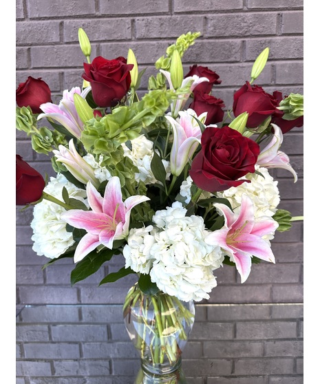 Stargazer lilies, long stem roses, white snapdragons and white hydrangea in a clear glass vase.