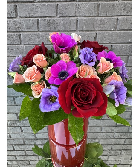 Flower arrangement of pink daisies, red spray roses and white daisies in a glass cube vase.