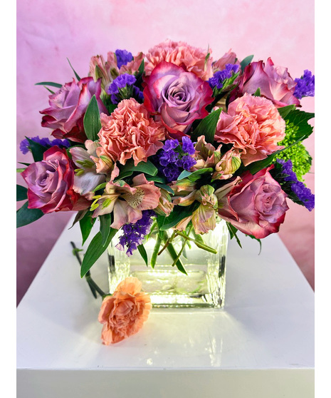 Pink carnations, lavender roses and alstroemeria in a clear glass cube vase with curly willow.